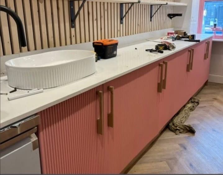 Commercial bar fit-out with fluted coral-pink cabinetry, brass handles, copper pendant lighting and herringbone flooring