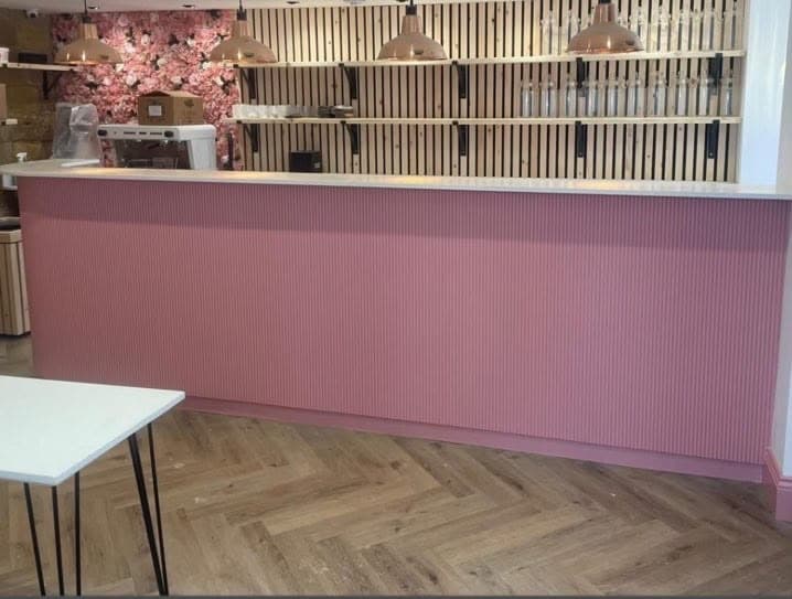 Close detail of the fluted coral-pink cabinetry and brass handles on the commercial bar fit-out, mid-installation