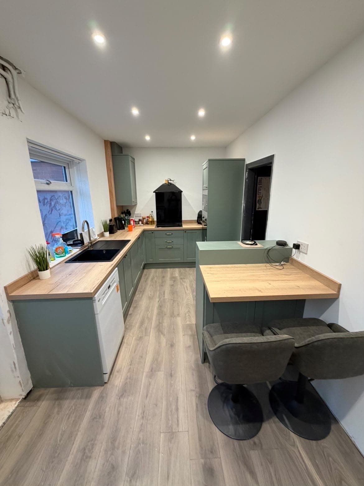 Fitted sage-green shaker-style kitchen with a central island breakfast bar, oak-effect worktops and integrated appliances