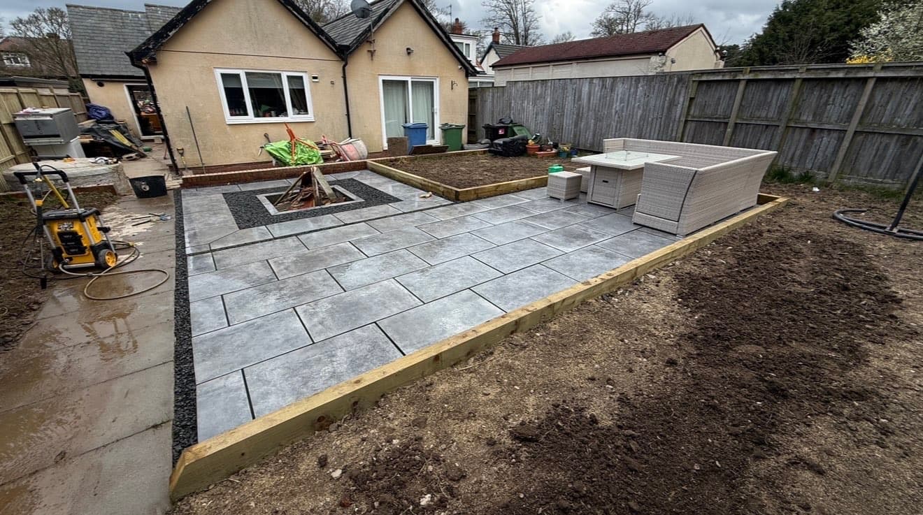 Newly laid grey porcelain-effect patio with a sunken fire pit and rattan corner seating, photographed before the surrounding garden was finished
