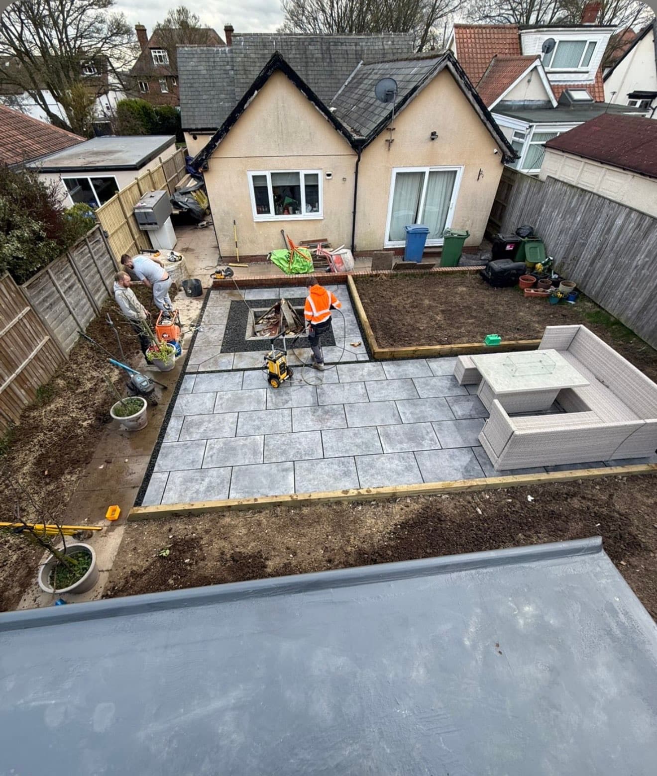 Elevated view of the finished patio and fire pit during final pressure-washing, with the newly turfed border alongside