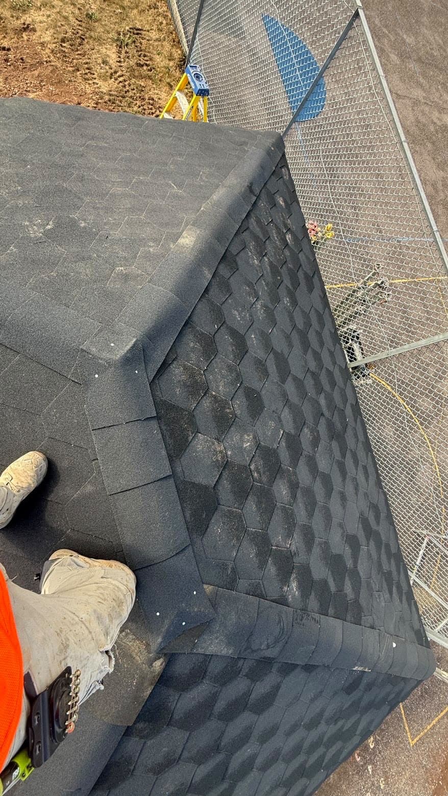 Roofer installing hexagonal-pattern roof shingles, working along the roof edge