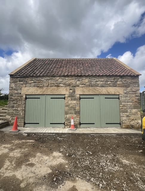 Stone-built rural outbuilding with a pair of sage-green ledged-and-braced double doors, finished with a tiled roof